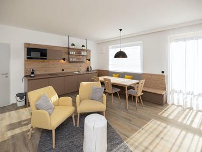 Helles, modernes Wohnzimmer mit Holzboden, gelben Sesseln, Eckbank und großem Fenster.