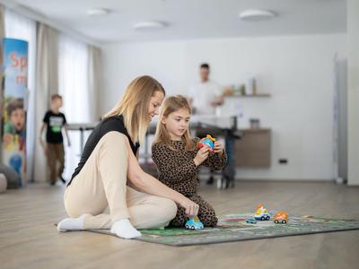 Zwei Mädchen sitzen auf dem Boden und spielen mit Spielzeugautos in einem hellen Raum.