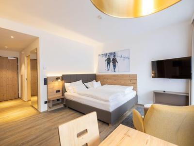 Modernes Hotelzimmer mit Doppelbett, Holzmöbeln, Fernseher und großem Fenster mit Vorhängen.