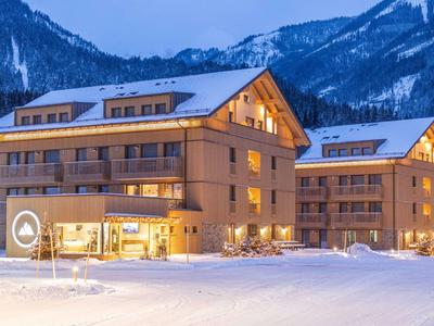 Beleuchtetes Hotel in verschneiter Berglandschaft bei Dämmerung.