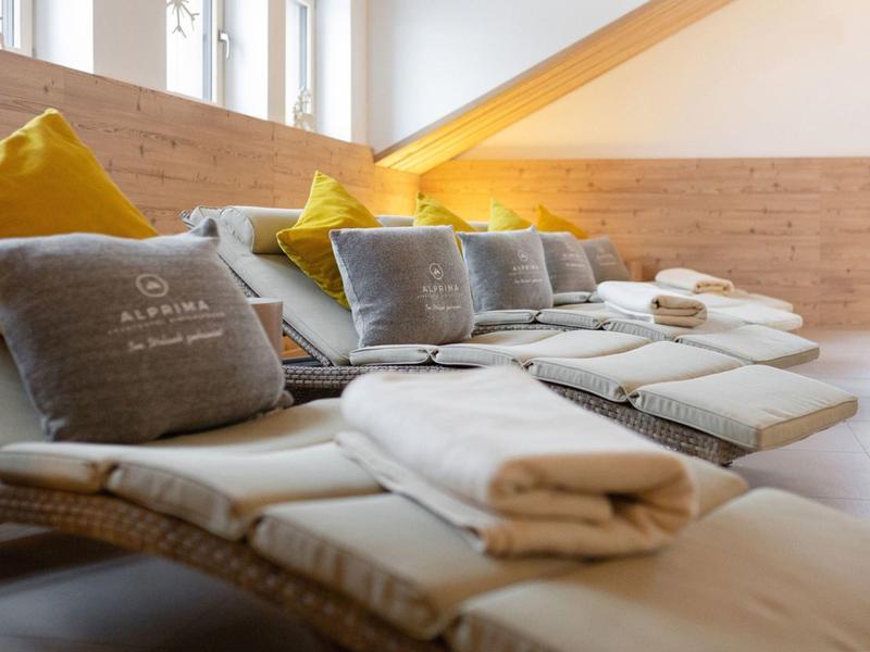 Gemütliche Liegen mit grauen Kissen und weißen Handtüchern in hellem Wellnessraum.
