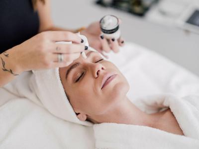 Frau erhält Gesichtskur, entspannt mit geschlossenen Augen, trägt weißen Handtuch-Turban.