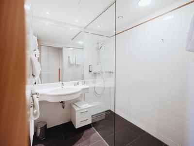 Modernes, helles Badezimmer mit Waschbecken, Spiegel und großer, ebenerdiger Dusche.