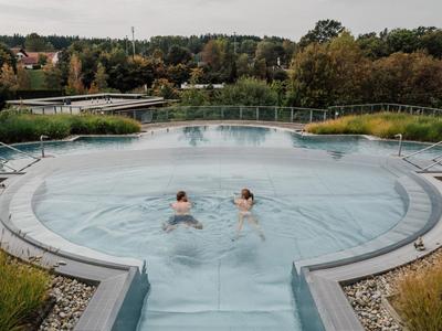 Zwei Personen entspannen im runden Außenwhirlpool mit Blick auf grüne Landschaft.