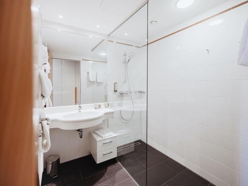 Helles, modernes Badezimmer mit Glasdusche, weißem Waschbecken und schwarzem Boden.