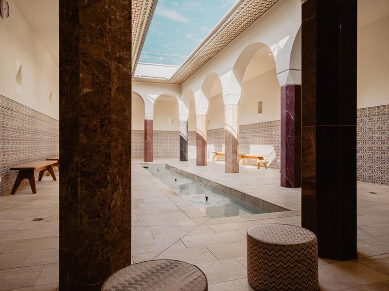 Innenhof mit langem Wasserbecken, Säulenbögen, Bank und einem blaue Himmel über dem Dach.