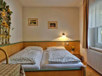 Gemütliches Doppelzimmer mit zwei Einzelbetten, Nachttischlampe und Fenster mit Vorhängen.