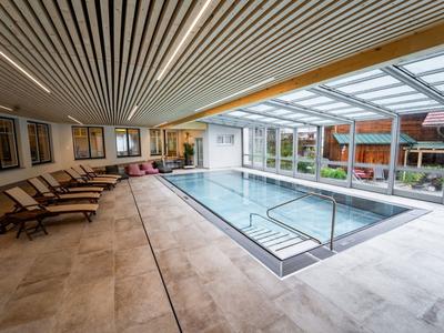 Moderner Hallenpool mit großen Fenstern, Liegestühlen und Holzlatten-Decke in hellem Raum.