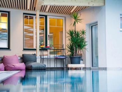 Innenpoolbereich mit klar Wasser, lila Sofas, großen Pflanzen und warm beleuchteten Fenstern.