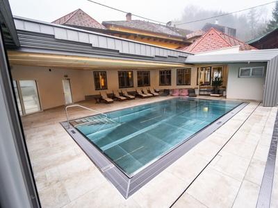 Moderner Innenpool mit Glaswand, Holzliegen und hellbeigen Fliesen in alpiner Umgebung.