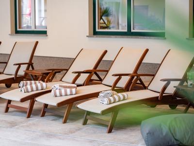 Vier Holzliegestühle mit weißen Kissen und gestreiften Handtüchern stehen nebeneinander auf Terrasse.