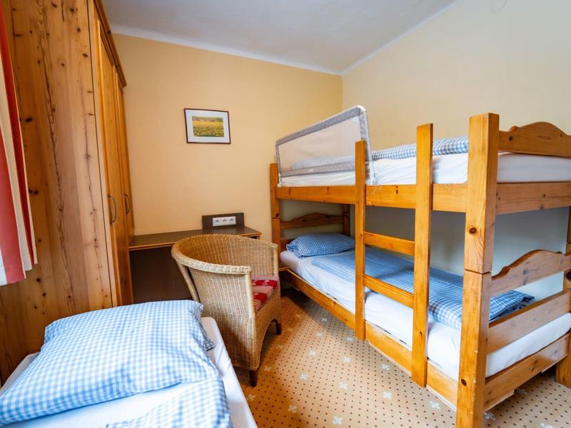 Kleines Zimmer mit Etagenbett und Einzelbett, Holzmöbeln, Schreibtisch und Stuhl.