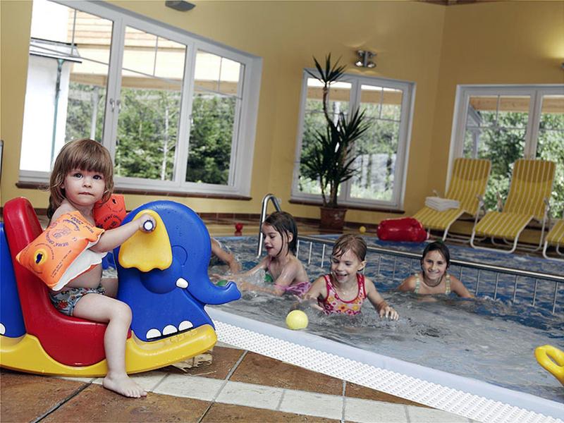 Kinder spielen im Hallenbad, eins sitzt auf einem blauen Papageien-Schwimmgerät.