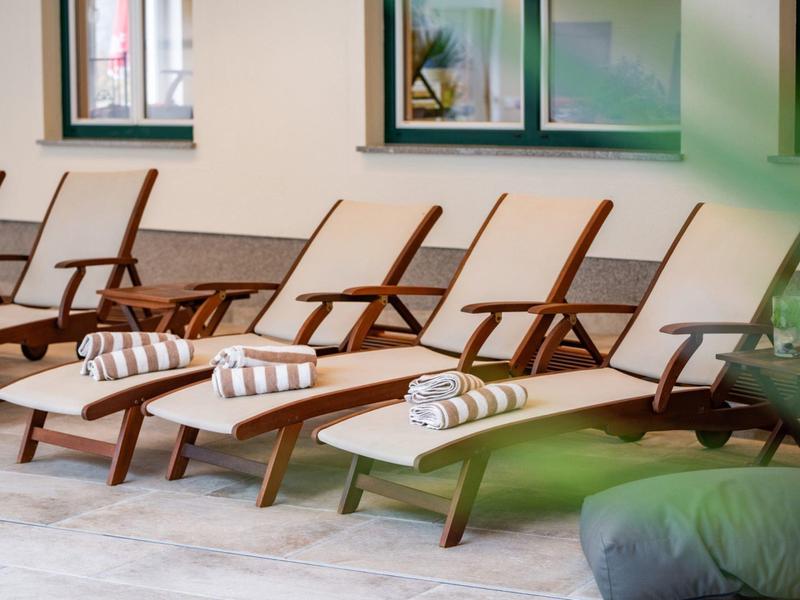 Vier Holzliegestühle mit weißen Kissen und gestreiften Handtüchern stehen nebeneinander auf Terrasse.