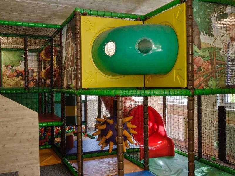 Indoor-Spielplatz mit Klettergerüst, grüner Röhre, roter Rutsche und weichem Bodenbelag.