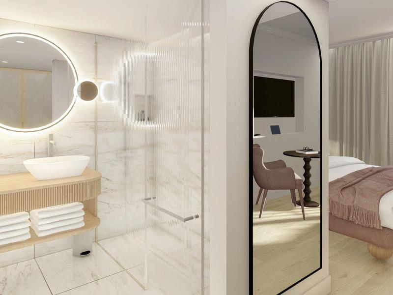 Helles Bad mit rundem Spiegel, Glasdusche und Holzwaschtisch neben hellem Schlafzimmer mit Doppelbett.