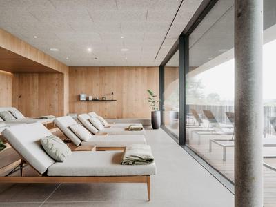 Moderner Ruhebereich mit Liegen, Holzwänden und bodentiefen Fenstern, viel Licht und klaren Linien.