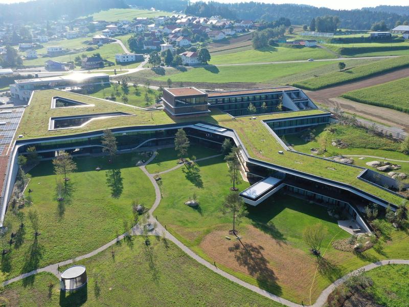 Großes, modernes Gebäude mit grünen Dächern und Wegen in ländlicher Umgebung bei Sonnenschein.