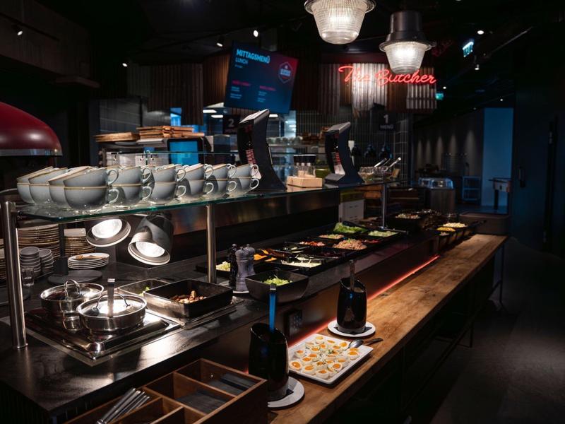 Buffet mit Geschirr, Schalen, Tellern und Speisen auf Holztheke in gedimmtem Licht.