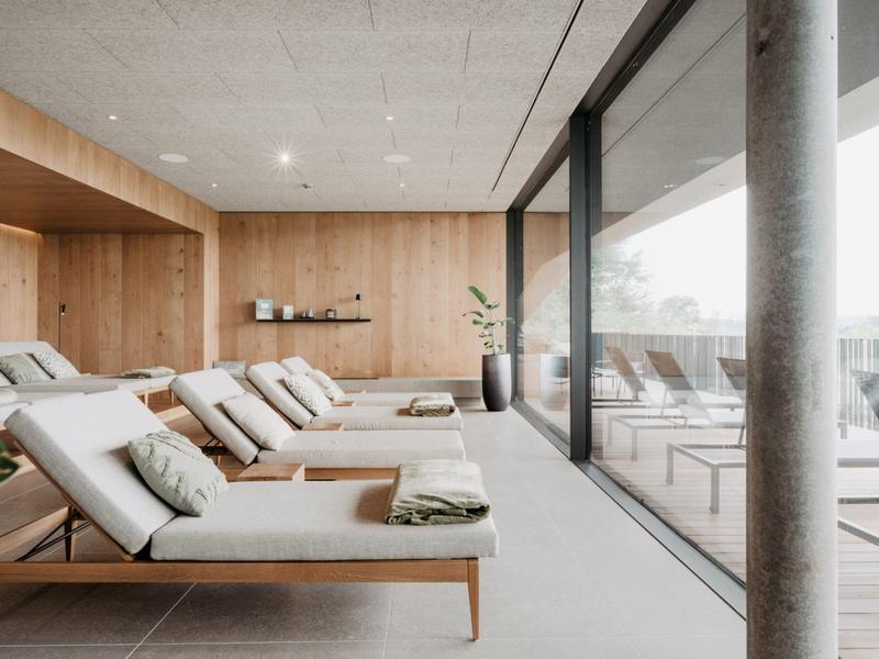 Moderner Ruhebereich mit Liegen, Holzwänden und bodentiefen Fenstern, viel Licht und klaren Linien.