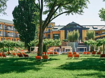 Moderner Hotelgarten mit grünen Rasenflächen, Bäumen und orangefarbenen Liegestühlen.