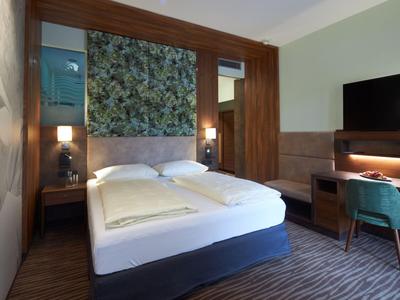 Modern eingerichtetes Hotelzimmer mit Doppelbett, TV und Arbeitsplatz.