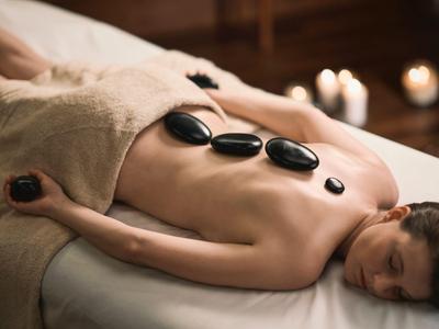Frau entspannt bei Hot Stone Massage im Spa mit warmem Licht und Kerzen.