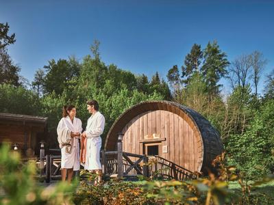 Zwei Personen in Bademänteln stehen vor einem runden Holzhotelzimmer in der Natur.