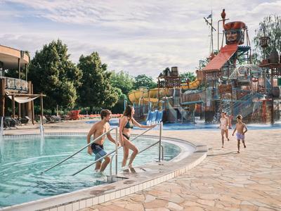 Kinder springen in einen flachen Pool in einem Wasserpark neben einem Hotel.