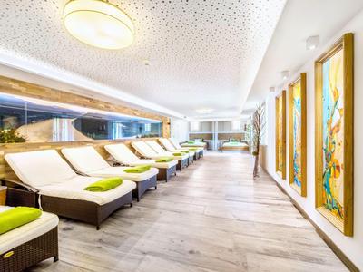 Heller Wellnessbereich mit Liegen, grünen Kissen und abstrakten Wandbildern auf hellem Boden.