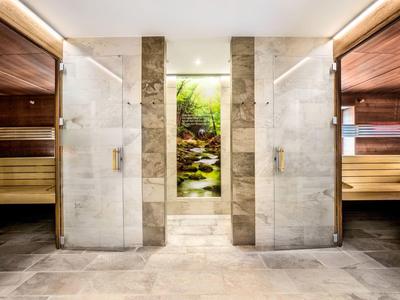 Moderner Wellness-Bereich mit zwei Glastür-Duschen und angrenzenden Holz-Saunen, zentral beleuchtet.