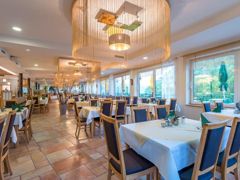 Großes Restaurant mit Tischen, grünen Stühlen, Holzboden und großen Fenstern mit Ausblick auf Garten.