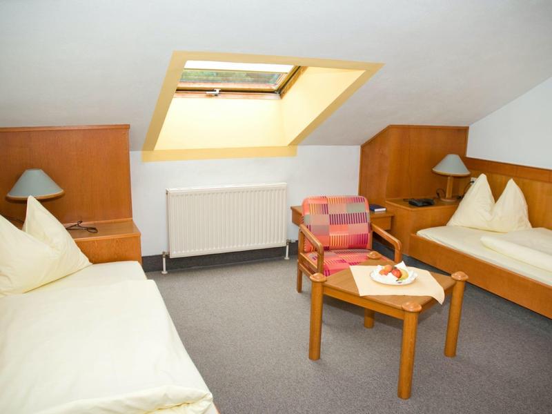 Einfaches Zimmer mit zwei Einzelbetten, Holzmöbeln, Dachfenster und kleinem Tisch mit Stühlen.