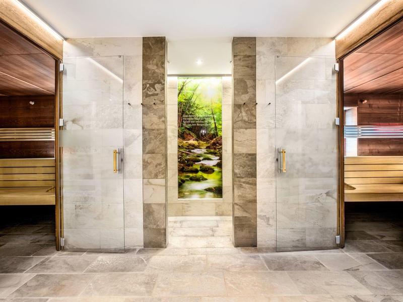 Moderner Wellness-Bereich mit zwei Glastür-Duschen und angrenzenden Holz-Saunen, zentral beleuchtet.