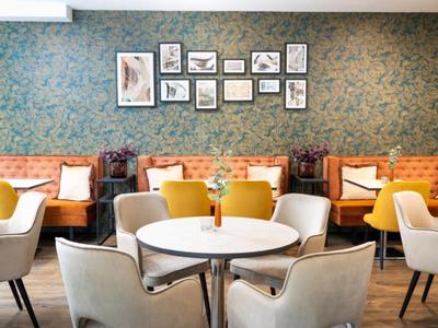 Nowoczesna jadalnia z okrągłymi stołami, wygodnymi krzesłami i dekoracjami ściennymi.