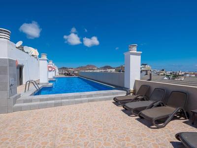 Terrazza sul tetto con piscina a sfioro e lettini sotto un cielo azzurro.