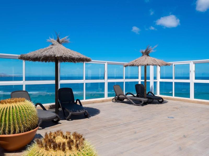 Terrazza con lettini, ombrelloni di paglia e cactus con vista sul mare blu.