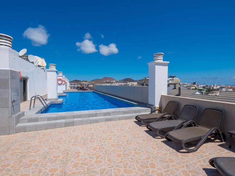 Terrazza sul tetto con piscina a sfioro e lettini sotto un cielo azzurro.