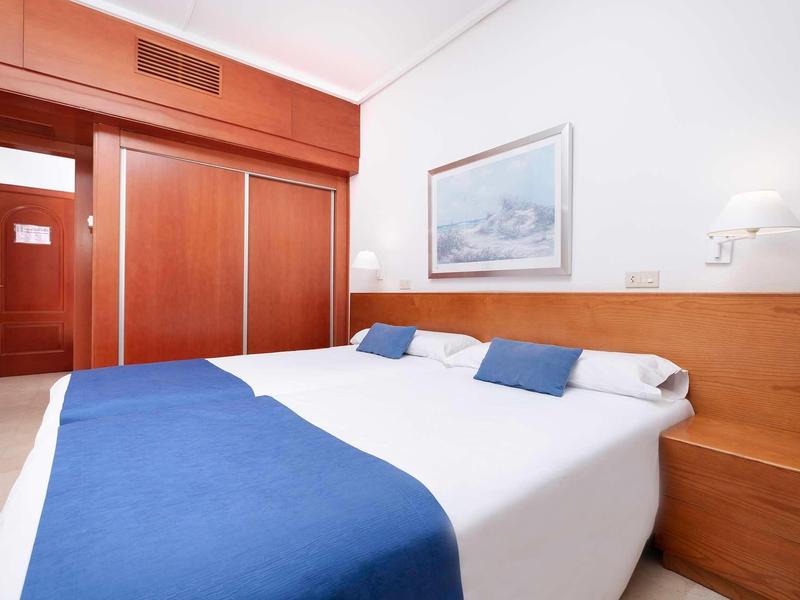 Camera d'hotel con letto grande, coperte blu, mobili in legno e semplice quadro a parete.