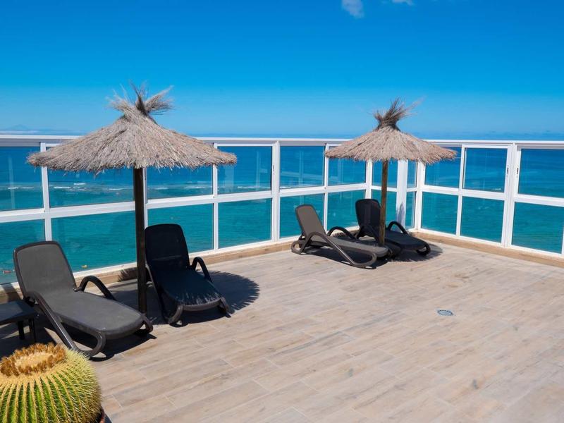 Terrazza panoramica con lettini e ombrelloni di paglia con vista sul mare blu.