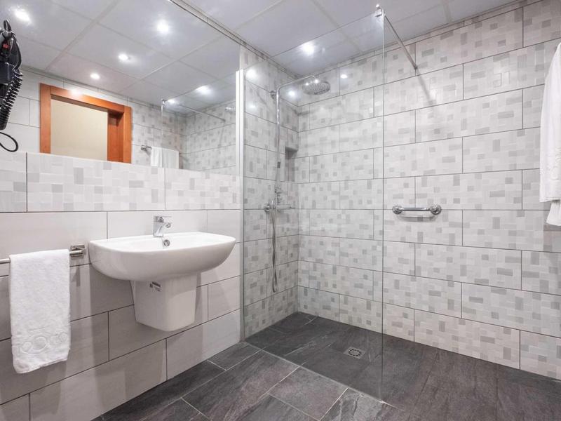 Bagno moderno con doccia a filo pavimento, grande specchio e lavabo bianco.