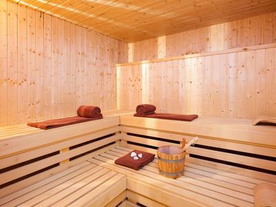 Sauna mit hellem Holz, zwei Liegen mit braunen Handtüchern und einem Holzeimer mit Schöpflöffel.
