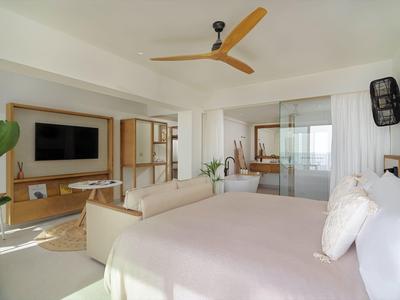 Helles Schlafzimmer mit großem Bett, Sofa, Deckenventilator und integriertem Wohnzimmerbereich.