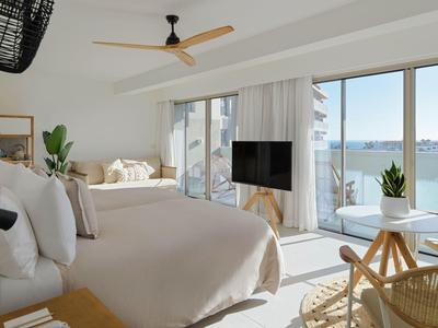 Helles Schlafzimmer mit großen Fenstern, Blick auf Wasser, modernem Ventilator und neutralen Farben.