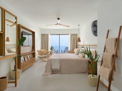 Helles Schlafzimmer mit großem Fenster, beige Bett, Pflanzen und Holz-Möbeln in modernem Stil.
