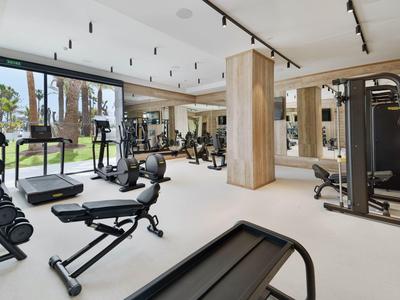 Moderner Fitnessraum mit Hantelbank, Laufband, Gewichten und großen Fenstern für viel Tageslicht.
