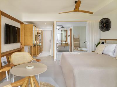 Camera d'hotel moderna con letto, TV, area salotto e bagno sullo sfondo.