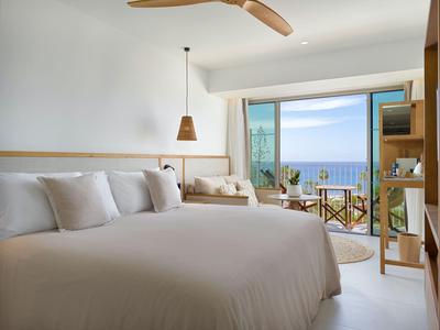 Camera d'hotel moderna con letto grande, zona salotto e vista mare attraverso una grande finestra.