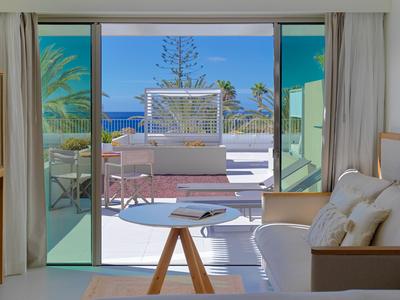 Soggiorno luminoso con divano e tavolo, vista sulla terrazza con mare e palme.
