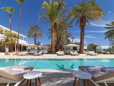 Piscina moderna dell'hotel con sdraio e palme sotto un cielo azzurro.